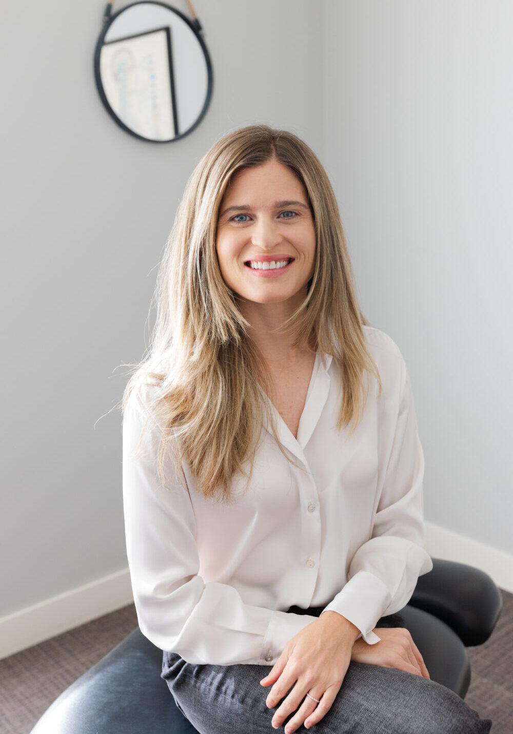 Dr. Rachael sitting on chiropractic table smiling at camera with arms gently crossed in lap.