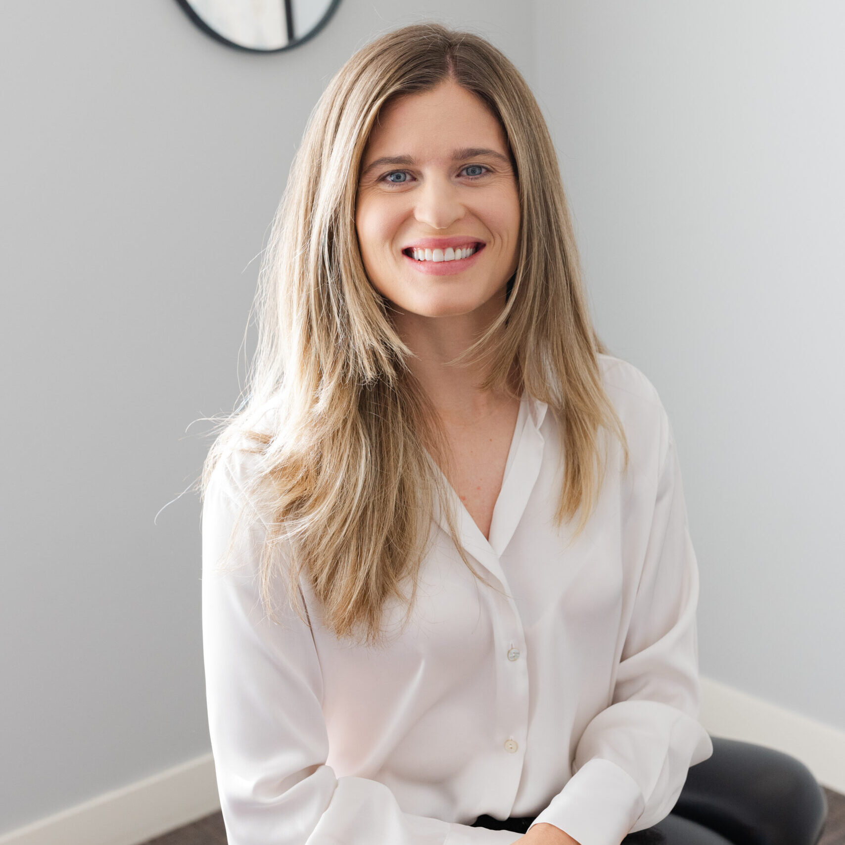 Dr. Rachael sitting on chiropractic table smiling at camera with arms gently crossed in lap.